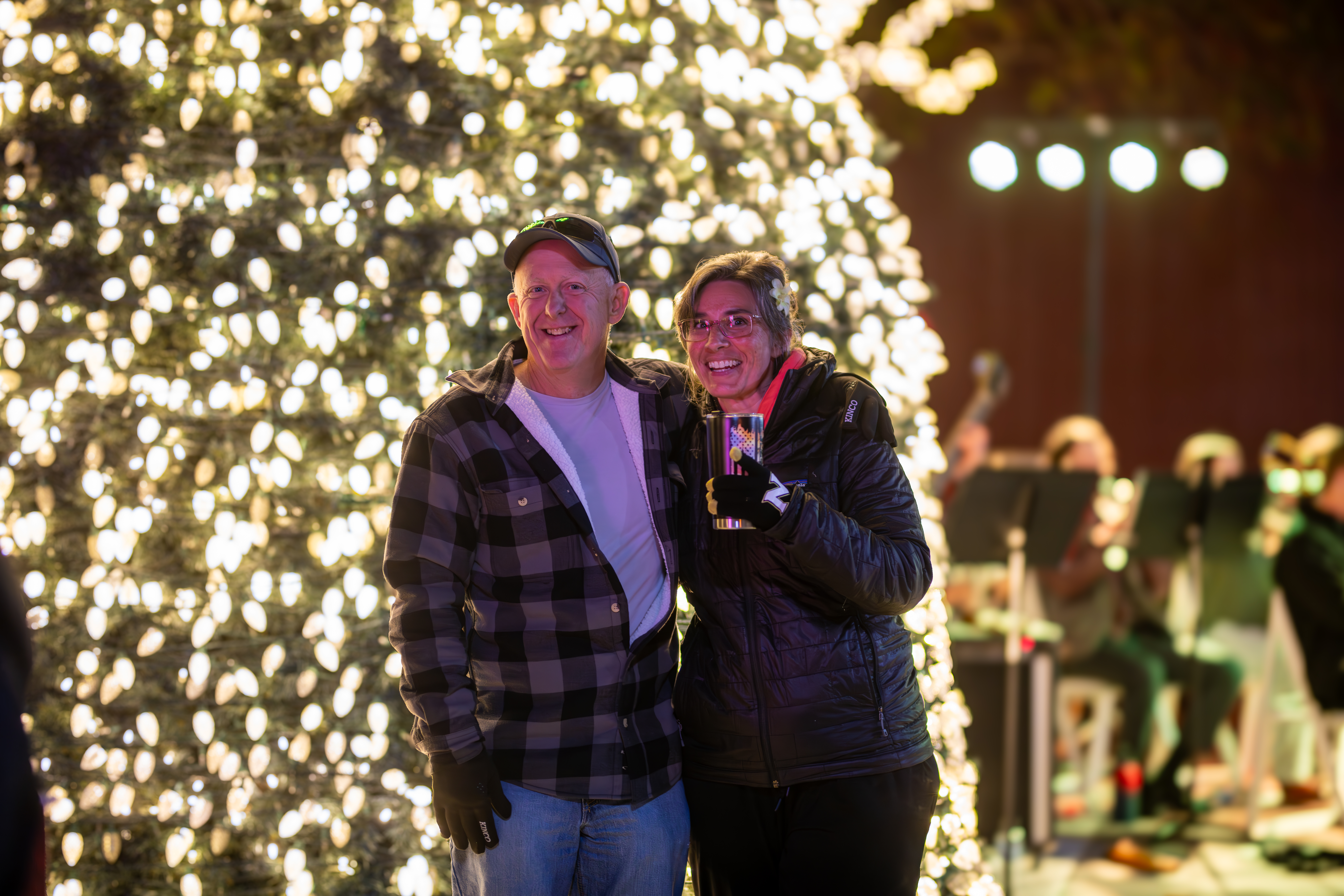 Couple Posing in front of the lighted christmas tree at pat coursey park with hot coco in hand.