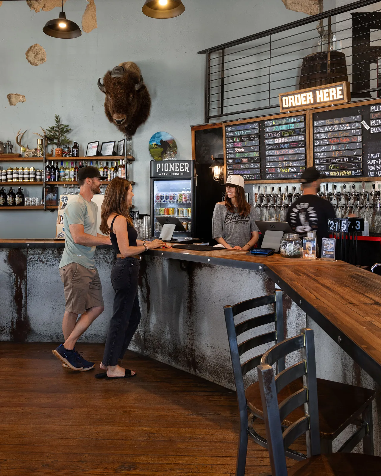 Customers ordering at the bar at Pioneer Tap House, under chalkboard beer menus and a row of taps